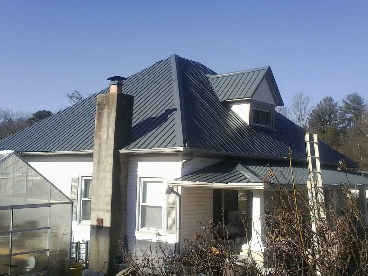 Dark blue standing seam metal roof on a white farmhouse with dormer — Slate & Tile Roof Repair by Roofing Brothers in Mathews
