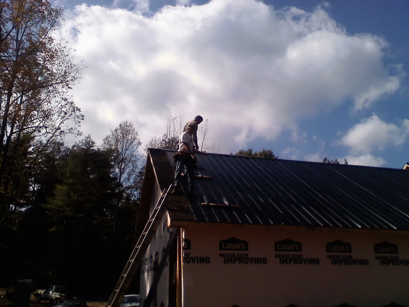 Roofer fastening dark metal panels high against a cloudy sky, from a Roof Inspection job in Mathews
