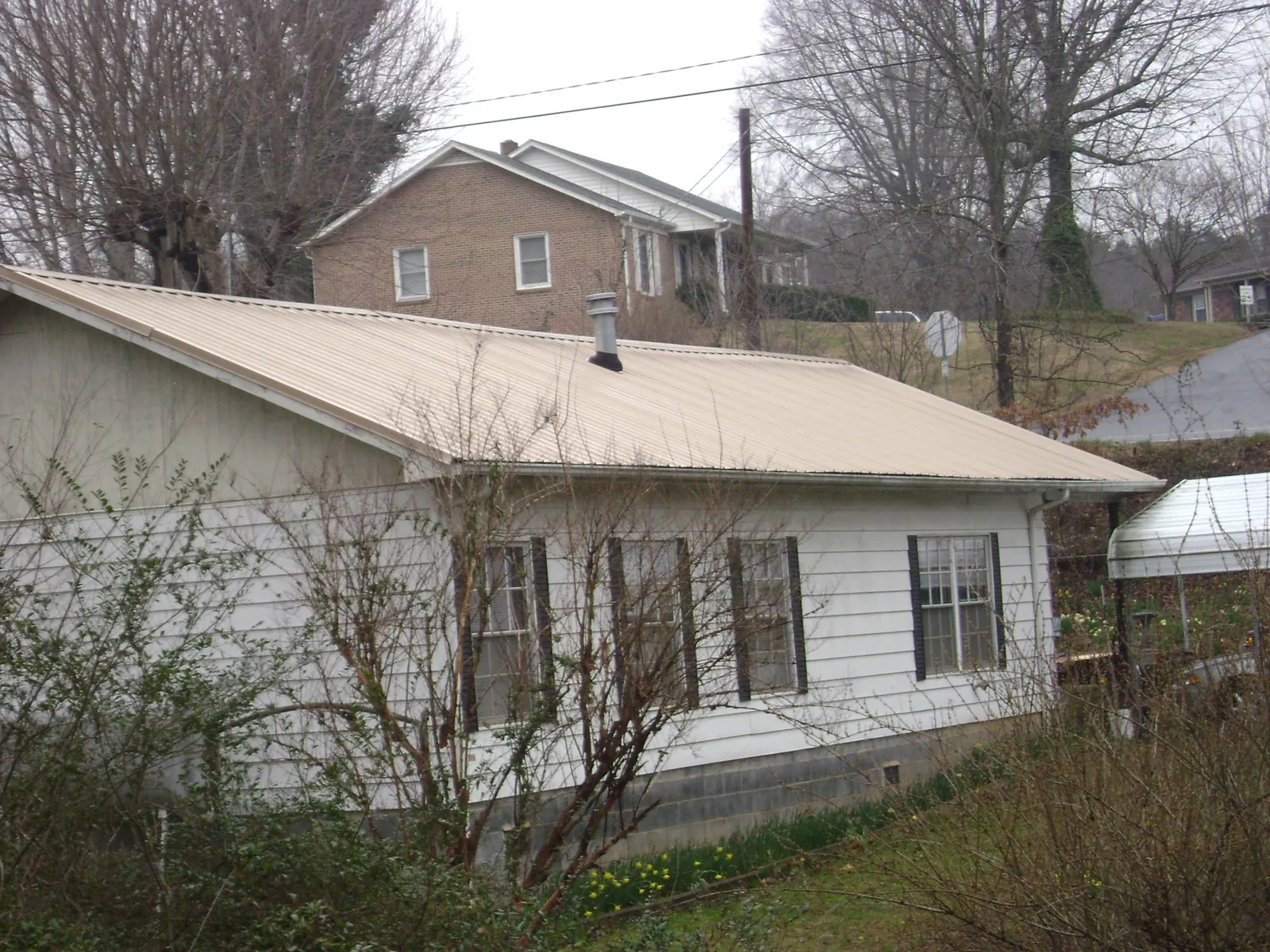 Tan metal roof on a white sided house set into a hillside — Commercial Roofing by Roofing Brothers in Mathews