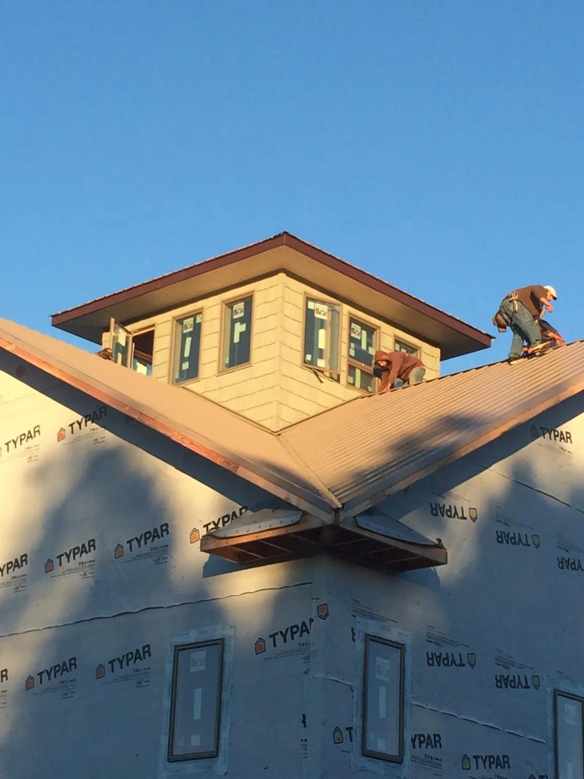 Roofers working around a rooftop cupola on a new metal roof at sunset — Roof Waterproofing in Mathews by Roofing Brothers